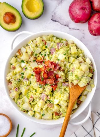 An overhead picture of the finished Avocado Potato Salad with a wooden spoon picking up some of the potato salad.