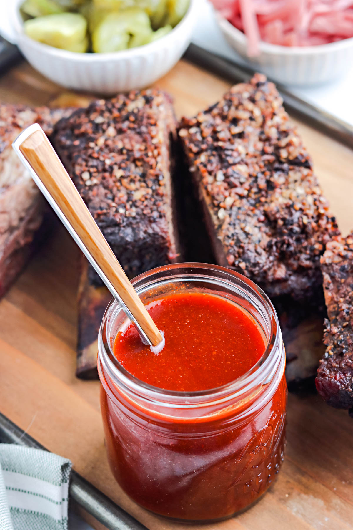 A jar of the finished Texas BBQ Sauce on a cutting bard with smoked beef ribs in the background.
