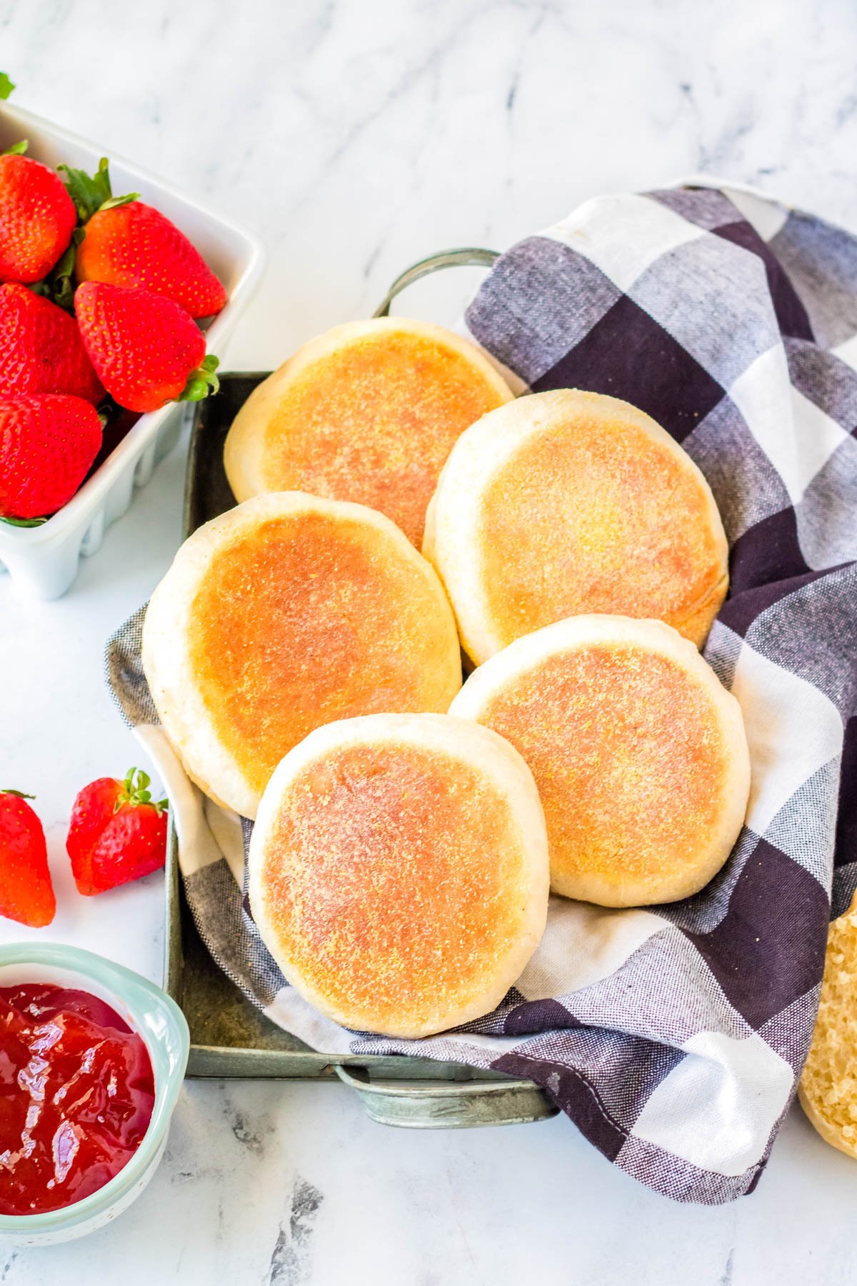 A basketful of 5 finished Homemade English Muffins with jam and butter nearby.