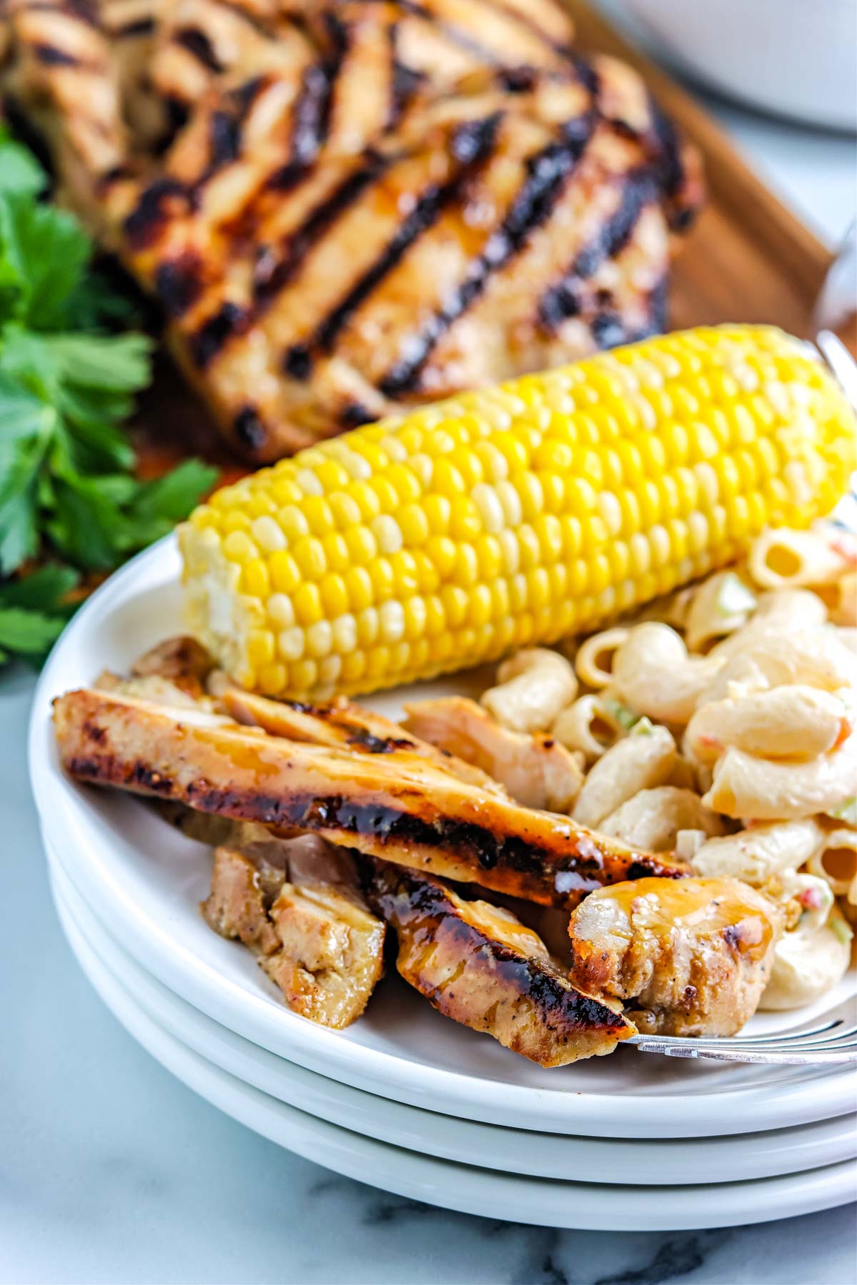 The finished grilled chicken thigh cut up and on a plate along with corn and macaroni salad.