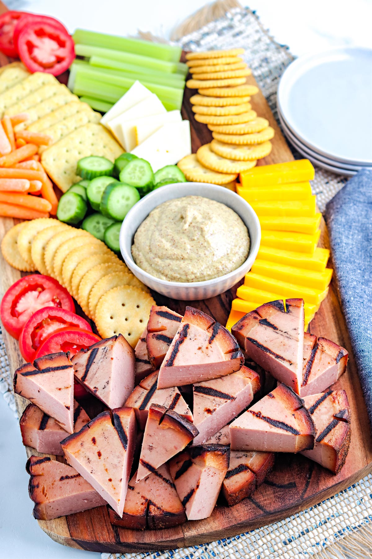 An overhead picture of a platter of the finished Smoke Bologna along with cheese, crackers, and sliced veggies on a wooden platter.