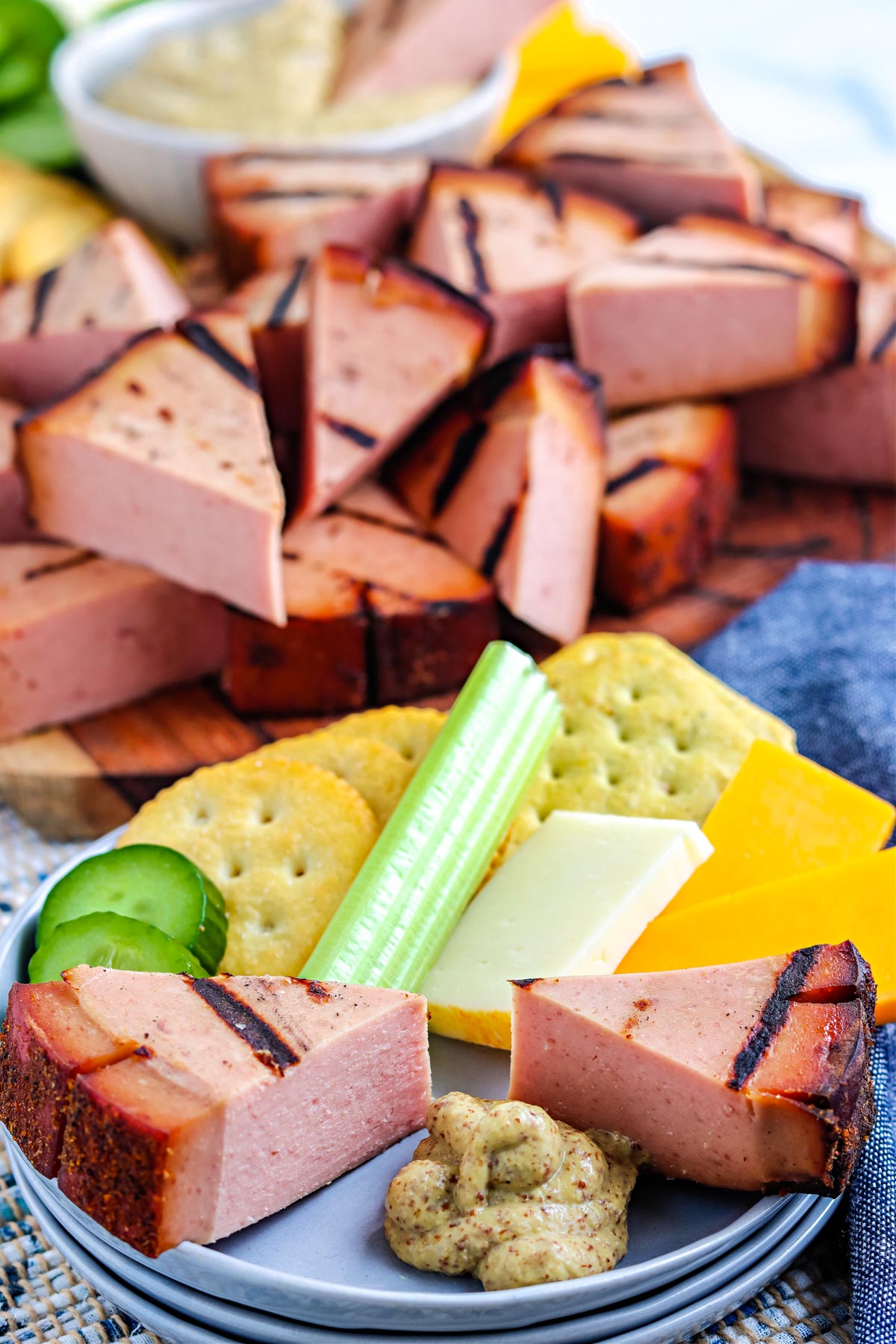 Pieces of the Smoked Bologna Chub on a plate with meat, cheese, crackers, and mustard.
