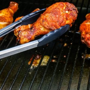 Smoked Chicken Drumsticks getting flipped with tongs.
