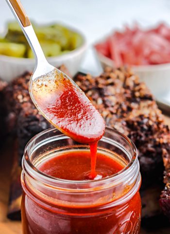 A spoon drizzling some of the Texas BBQ Sauce from a glass jar.