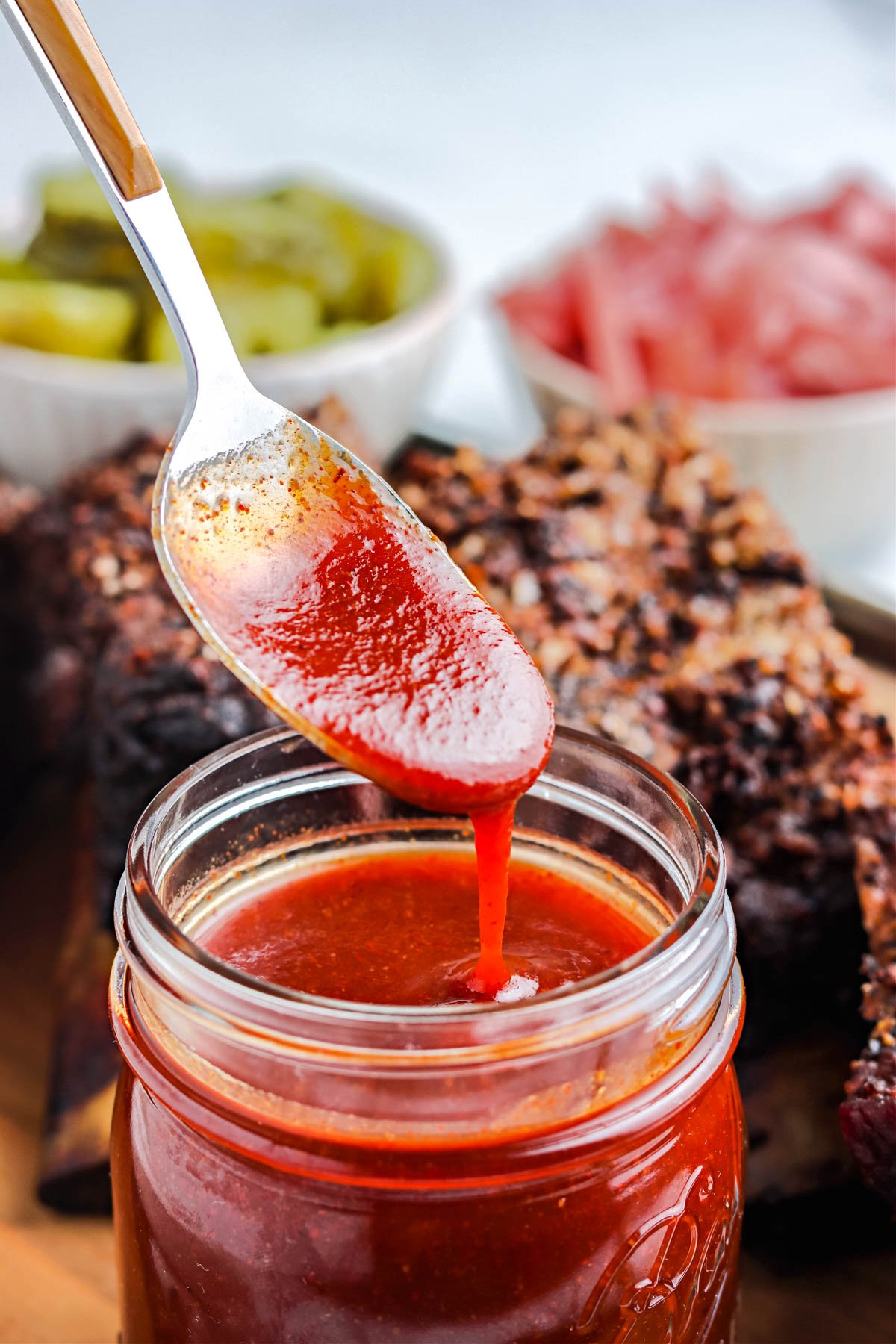 A spoon drizzling some of the Texas BBQ Sauce from a glass jar. 