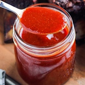 A spoon picking up some of the Texas Style BBQ Sauce from a glass jar.