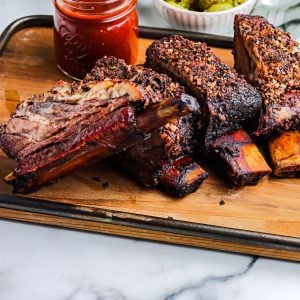 Beef ribs that have been smoked on a wooden cutting board.