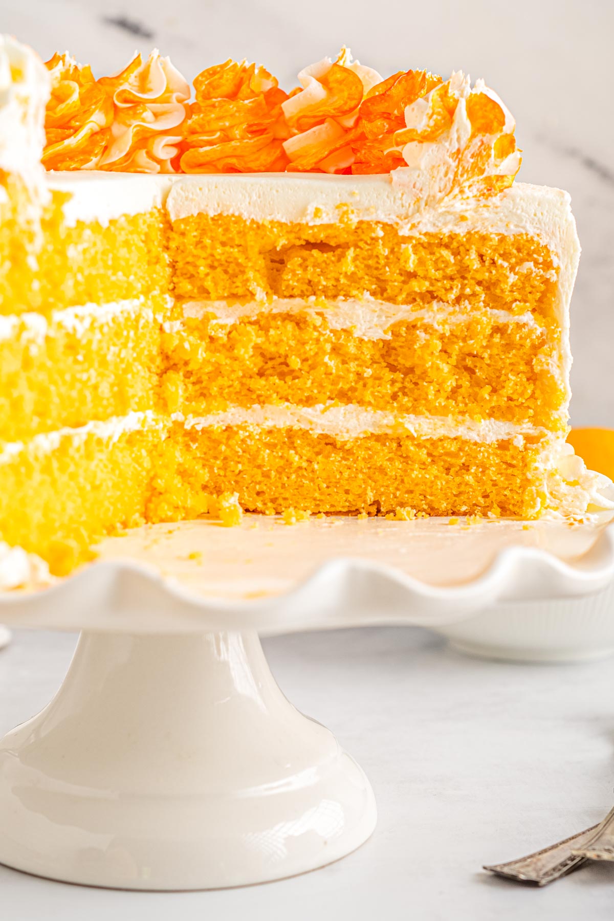 The finished Orange Creamsicle Cake made with Jello on a cake stand that has been cut into so you can see the layers.