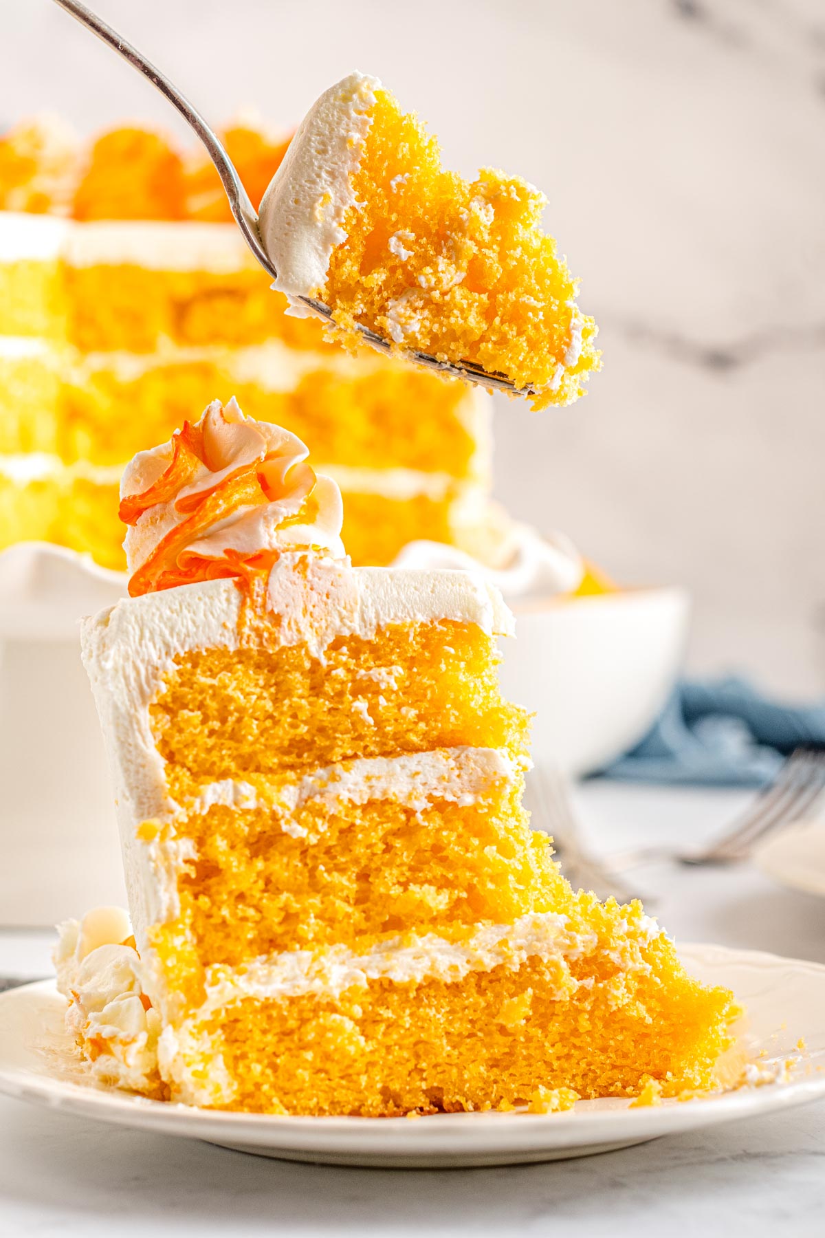 A slice of the finished Orange Dreamsicle Cake on a white plate with a fork digging into the cake.