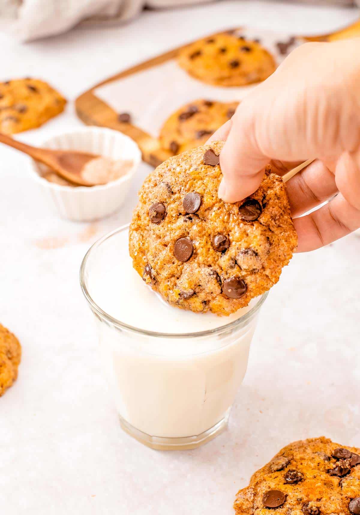 A Chewy Pumpkin Chocolate Chip Cookies being dunked into a glass of milk.
