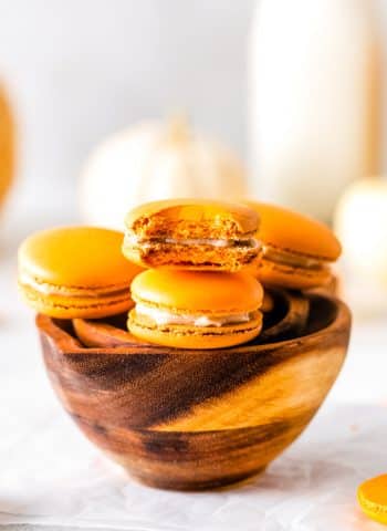 A bowl full of the finished Pumpkin Spice Macarons, one with a bite taken out of them.