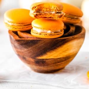 A close up picture of the finished Pumpkin Spice Macarons in a wood bowl.