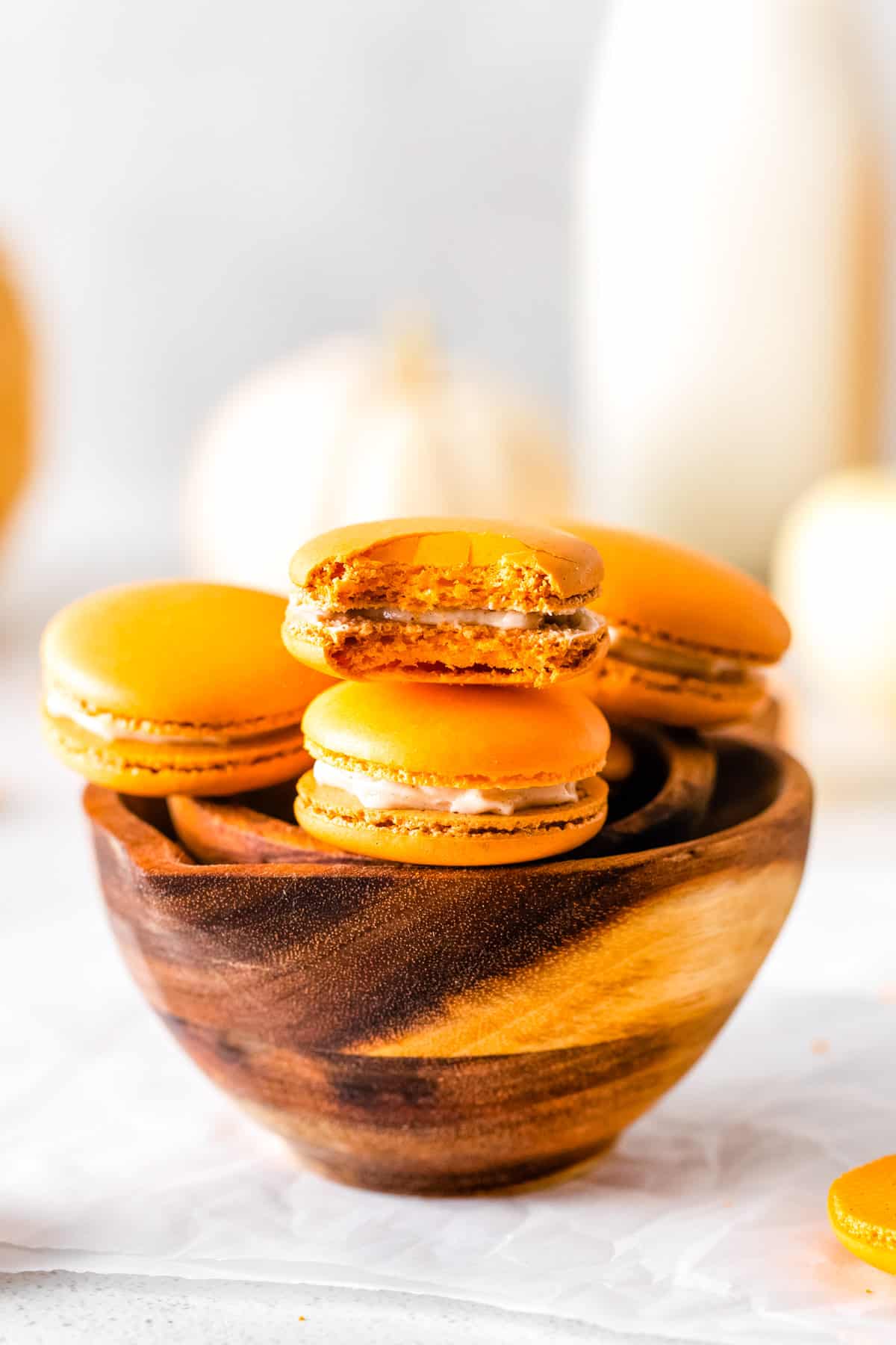 A bowl full of the finished Pumpkin Spice Macarons, one with a bite taken out of them. 
