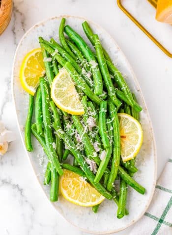 The finished Air Fryer Green Beans on a white platter garnished with Parmesan and lemon wedges.