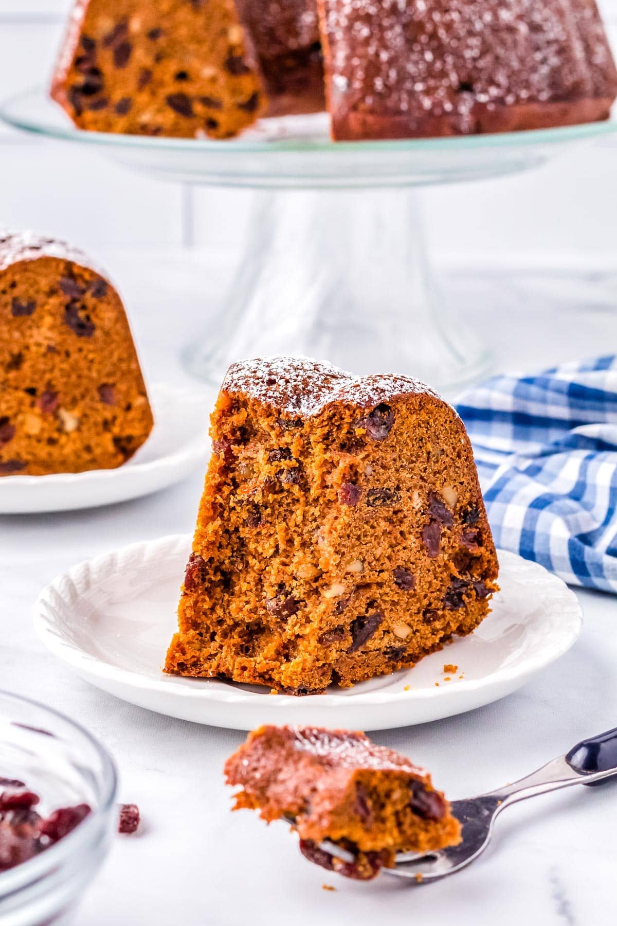 A slice of the Raisin Cake recipe on a white plate and cut into with a fork.