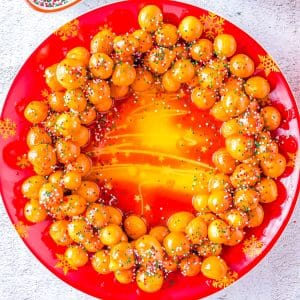A close up picture of the finished Struffoli recipe on a red plate.