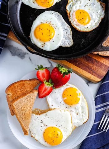 An overhead picture of fried eggs on a white plate and in an iron skillet.