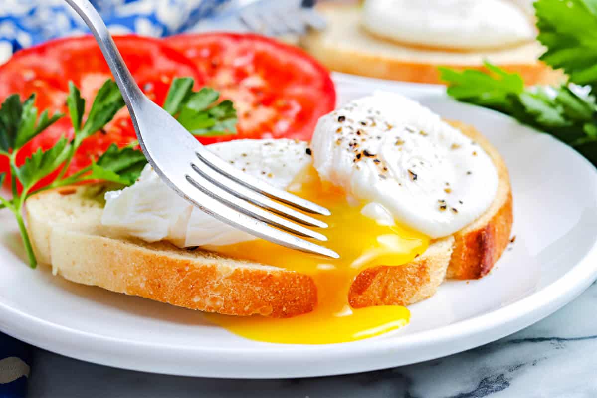 A fork breaking open a poached egg.