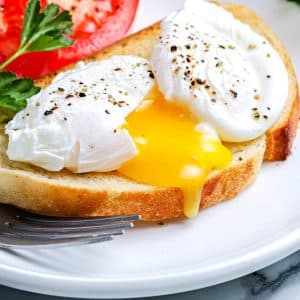 A close up picture of a poached egg split open on a piece of toast.