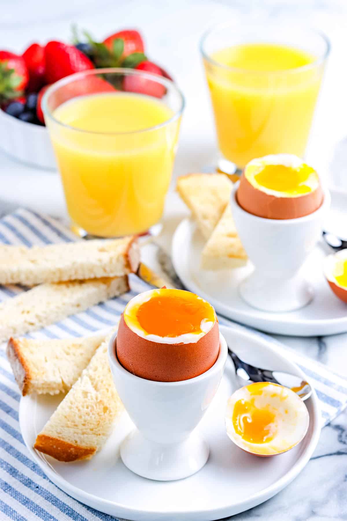 Soft Boiled Eggs in egg cups with toast for dipping on a white plate.