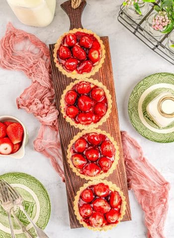 An overhead picture of four Strawberry Tartlets on a wooden serving board.