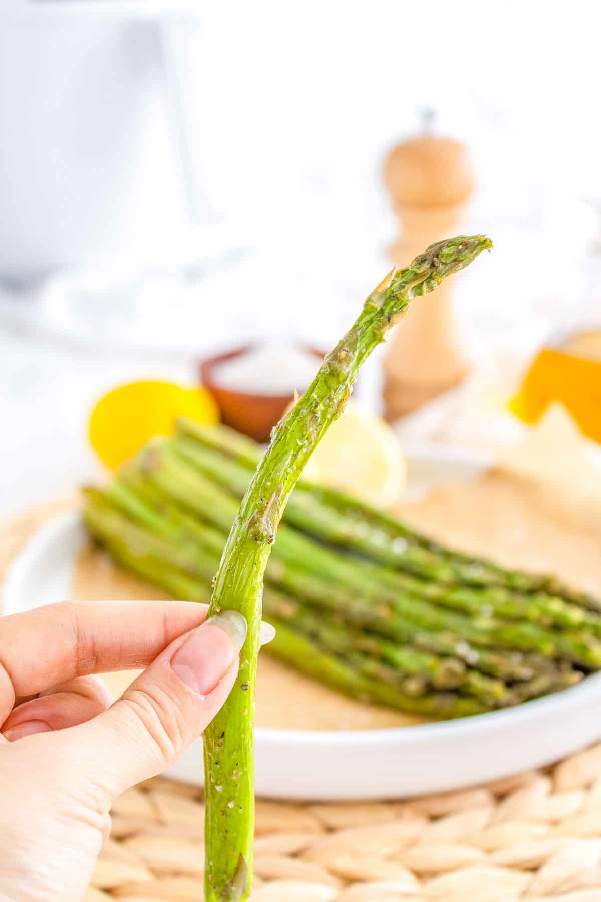 A hand picking up an air fried asparagus spear so you can how perfectly cooked it is.