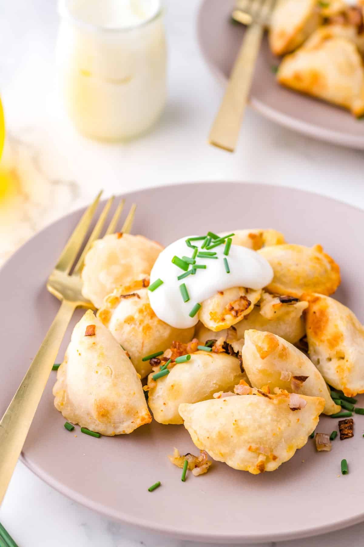 The finished Air Fryer Pierogies on a serving plate with sour cream and chives.