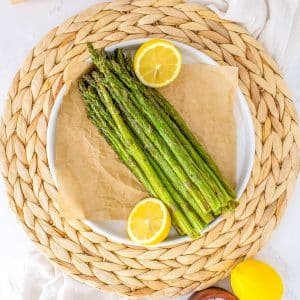 Asparagus made in an air fryer on a white serving platter with lemons.