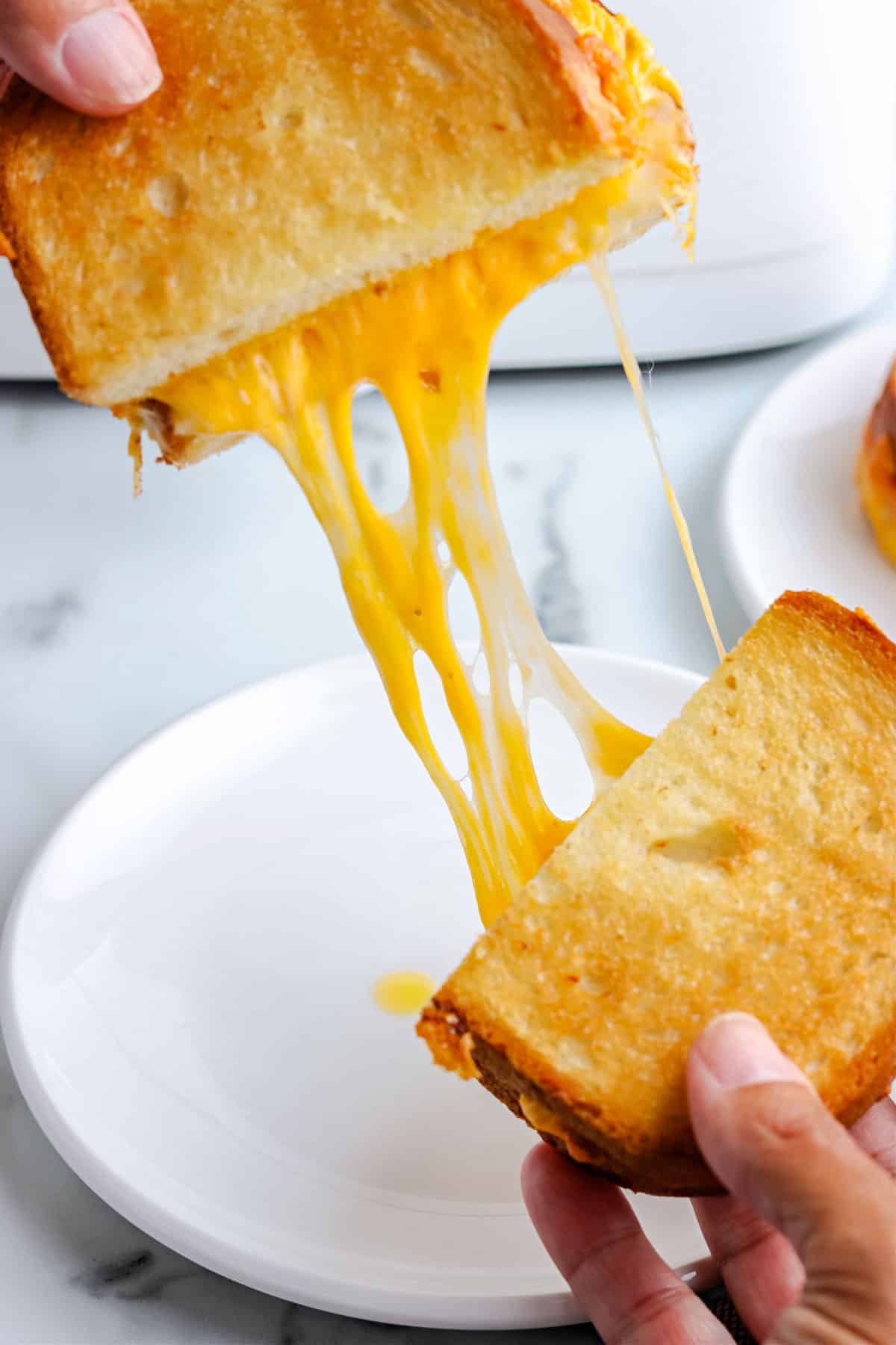 A grilled cheese cut in half and a long line of stretchy cheese coming from it.