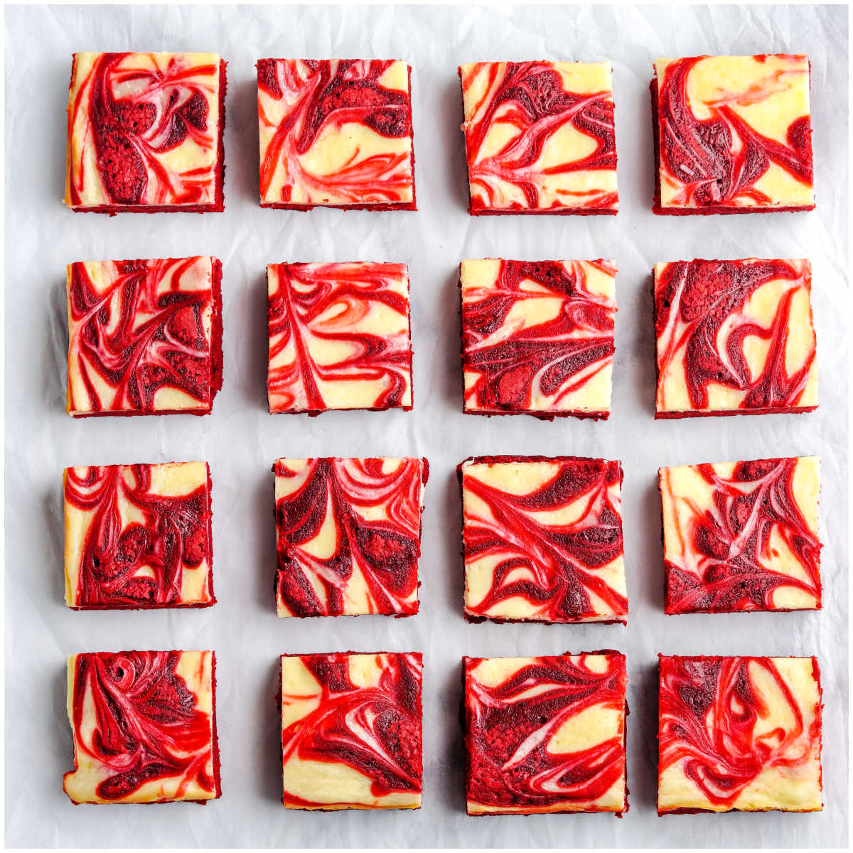 Sixteen red velvet brownies arranged in a grid to showcase the vibrant red and white cream cheese swirled tops.
