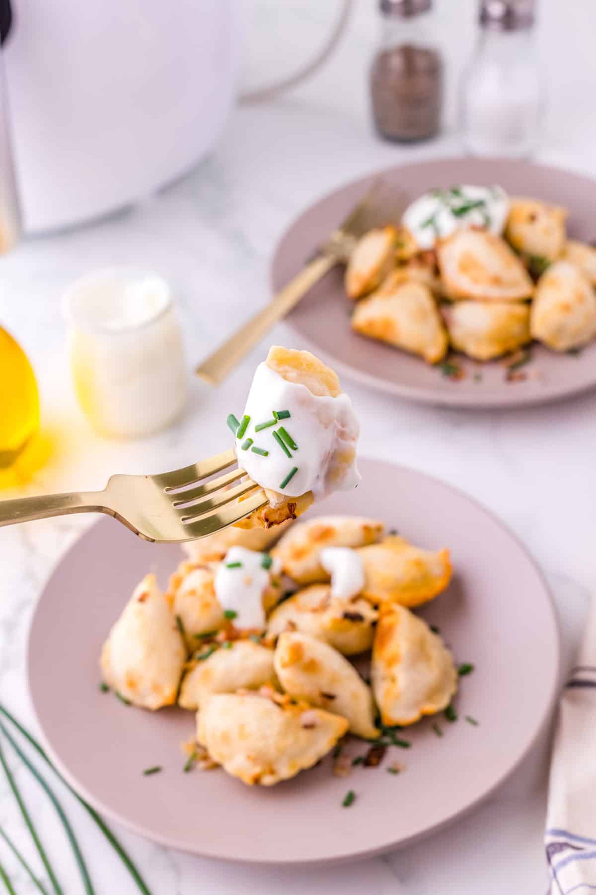 A fork picking up a pierogi with some sour cream on it.