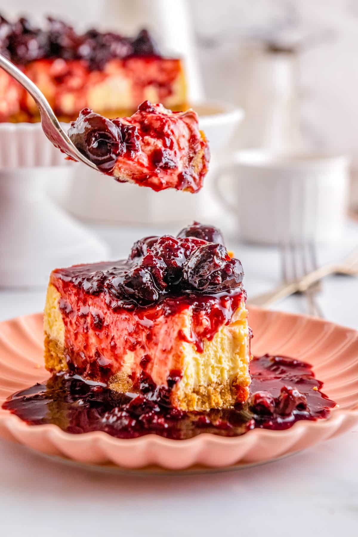 A fork taking a forkful of a slice of a Homemade Cherry Cheesecake.