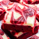 A close up of stacked red velvet brownies showing the creamy white cheesecake swirl and deep red brownie layers.