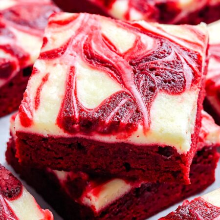 A close up of stacked red velvet brownies showing the creamy white cheesecake swirl and deep red brownie layers.