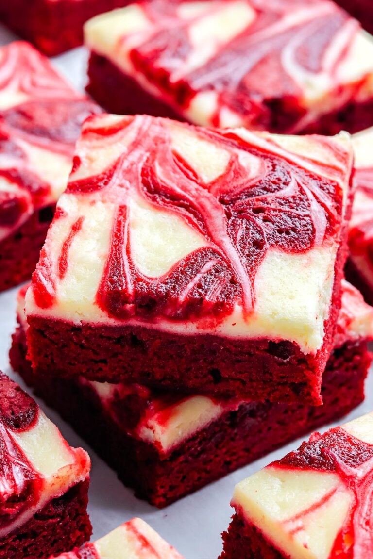 A close up of stacked red velvet brownies showing the creamy white cheesecake swirl and deep red brownie layers.