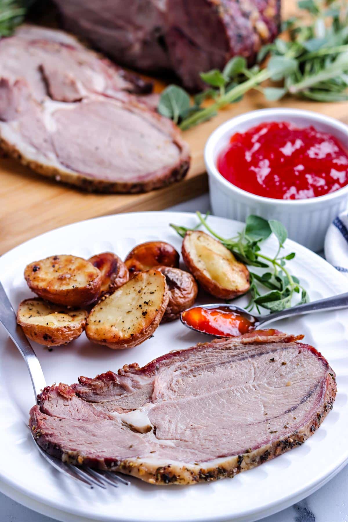 A slice of the Smoked Lamb on a white plate with pepper jelly and roasted potatoes.