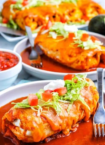 A Wet Burrito on a plate that's garnished with shredded lettuce, tomatoes, and sour cream.