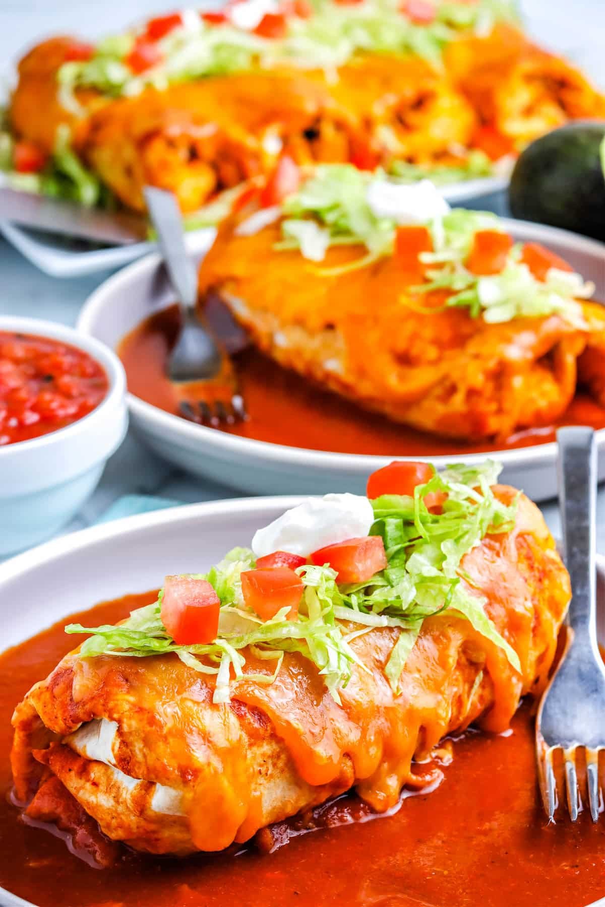 A Wet Burrito on a plate that's garnished with shredded lettuce, tomatoes, and sour cream. 