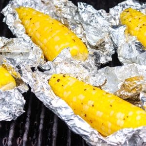 A close up picture of grilled corn in foil on the grill.