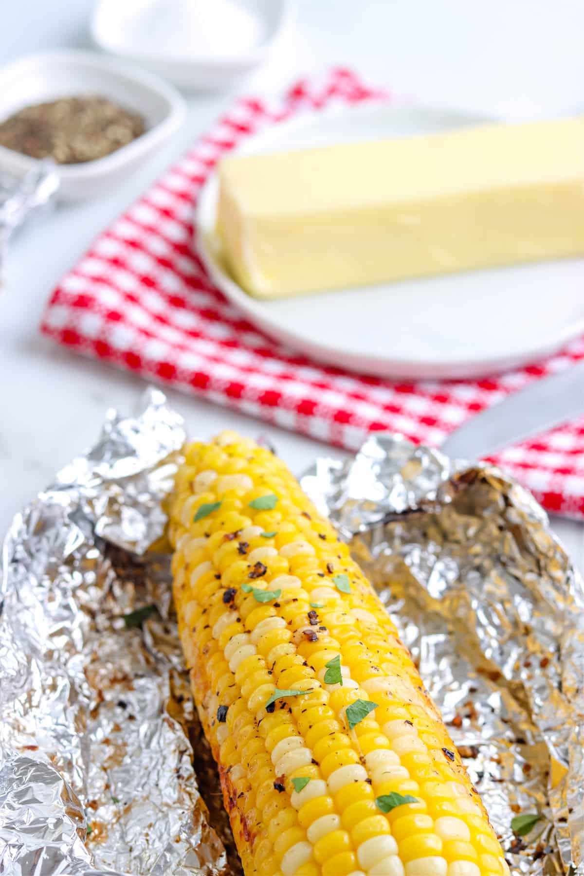 A close up picture of grilled corn on the cob in foil all unwrapped and ready to eat