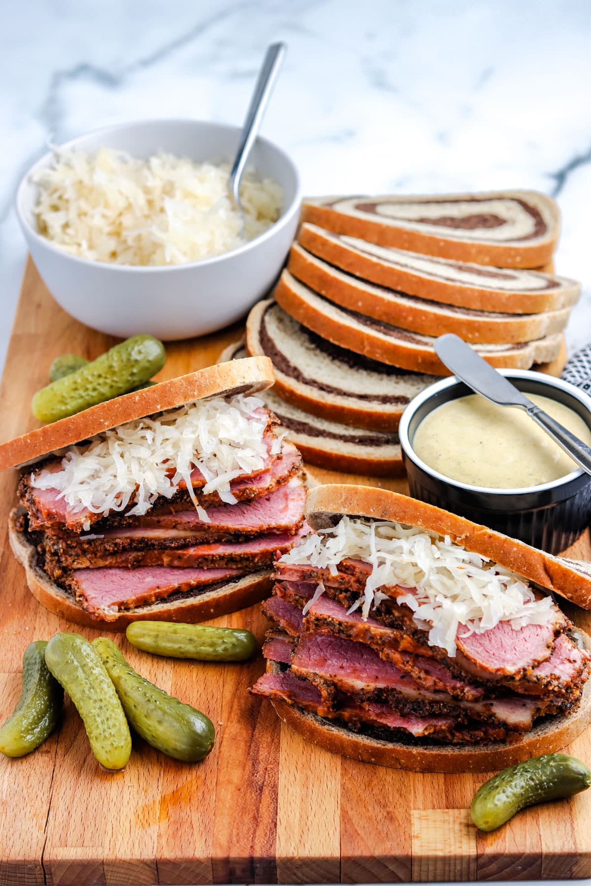 Assembled pastrami sandwiches on a wood cutting board.