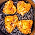 Four cooked chicken thighs in an air fryer.