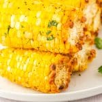 The finished corn on the cob made in an air fryer stacked on a white platter.