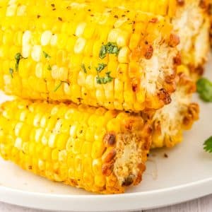 The finished corn on the cob made in an air fryer stacked on a white platter.