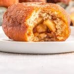 An apple donut that's been bitten into so you can se the apple filling.