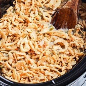 A serving spoon scooping up some green bean casserole from a slow cooker.