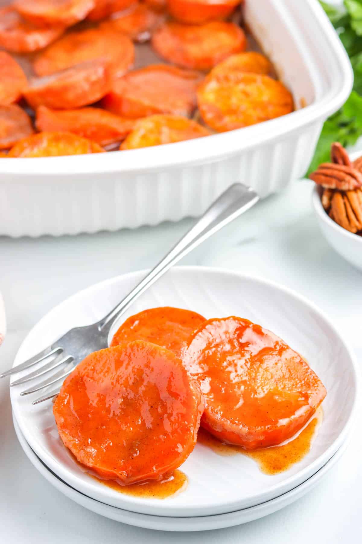 Some slices of the finished Southern candied yams recipe on a white plate with a fork.