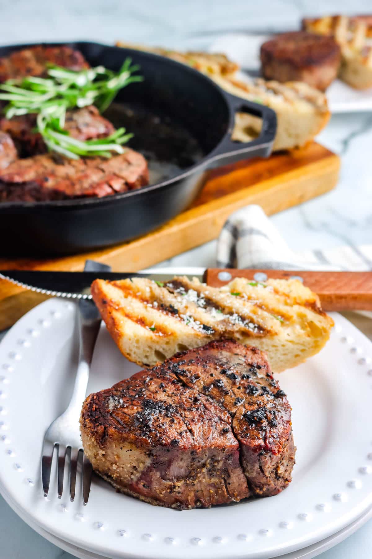 A smoked filet mignon on a white plate with garlic bread.