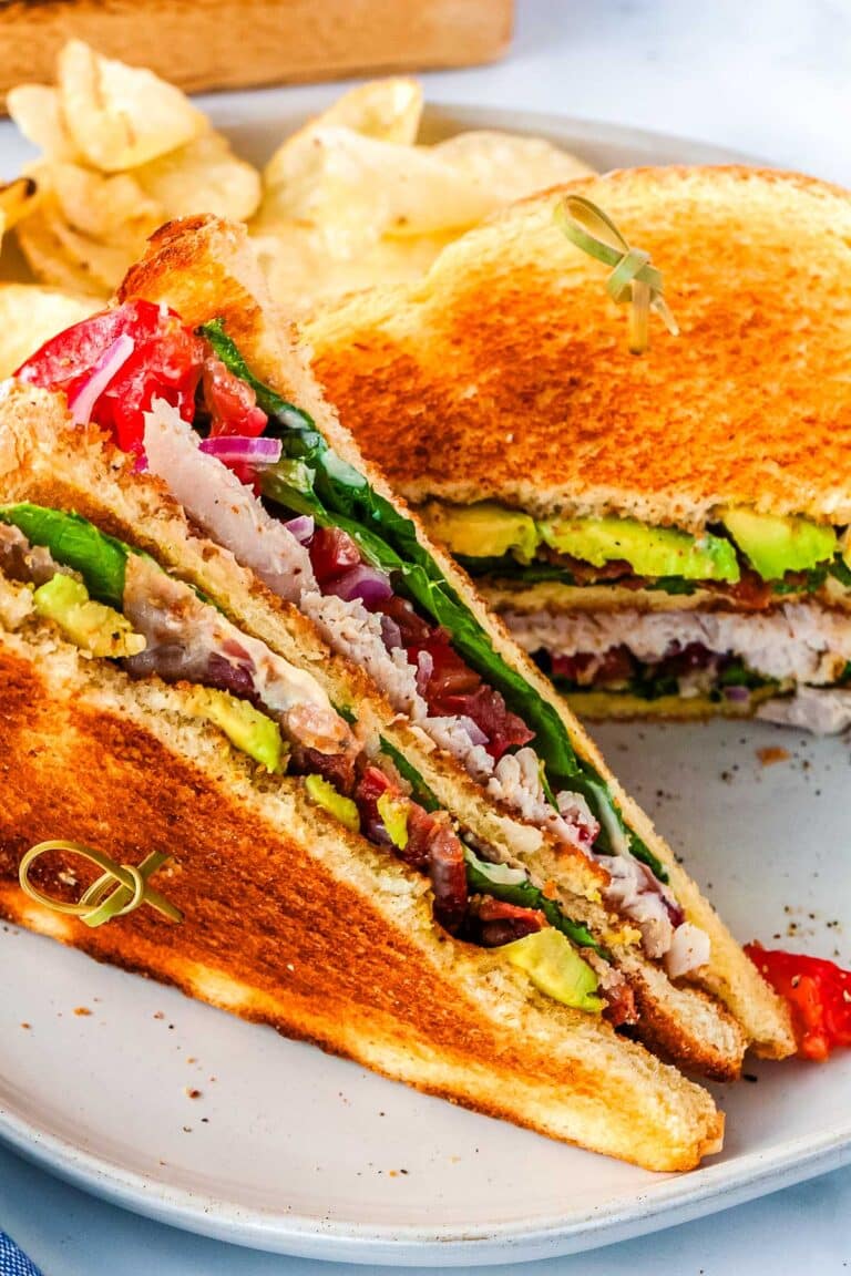 A chicken club sandwich cut in half and on a white plate.