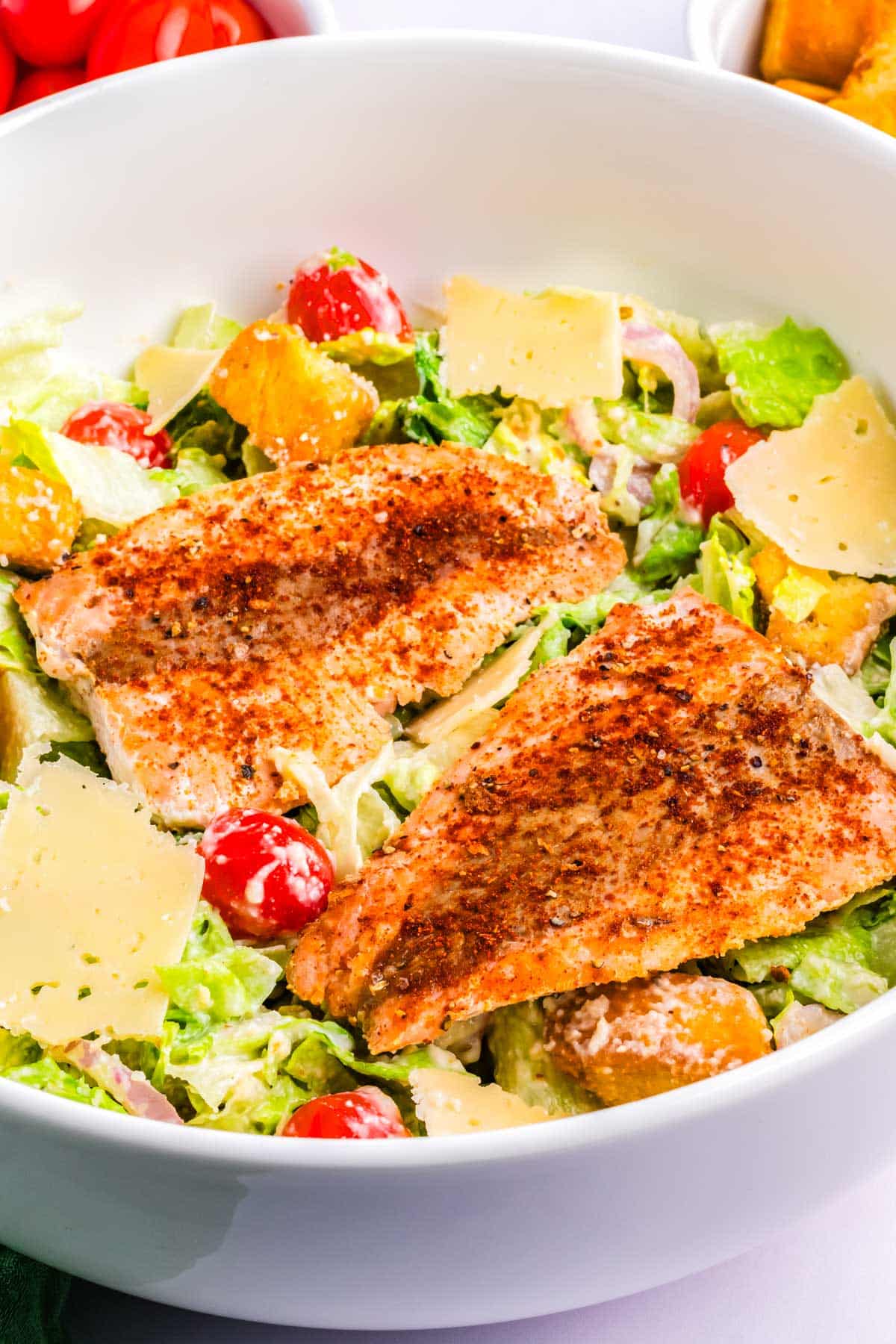 Salmon laying on top of a Caesar salad and garnished with Parmesan.